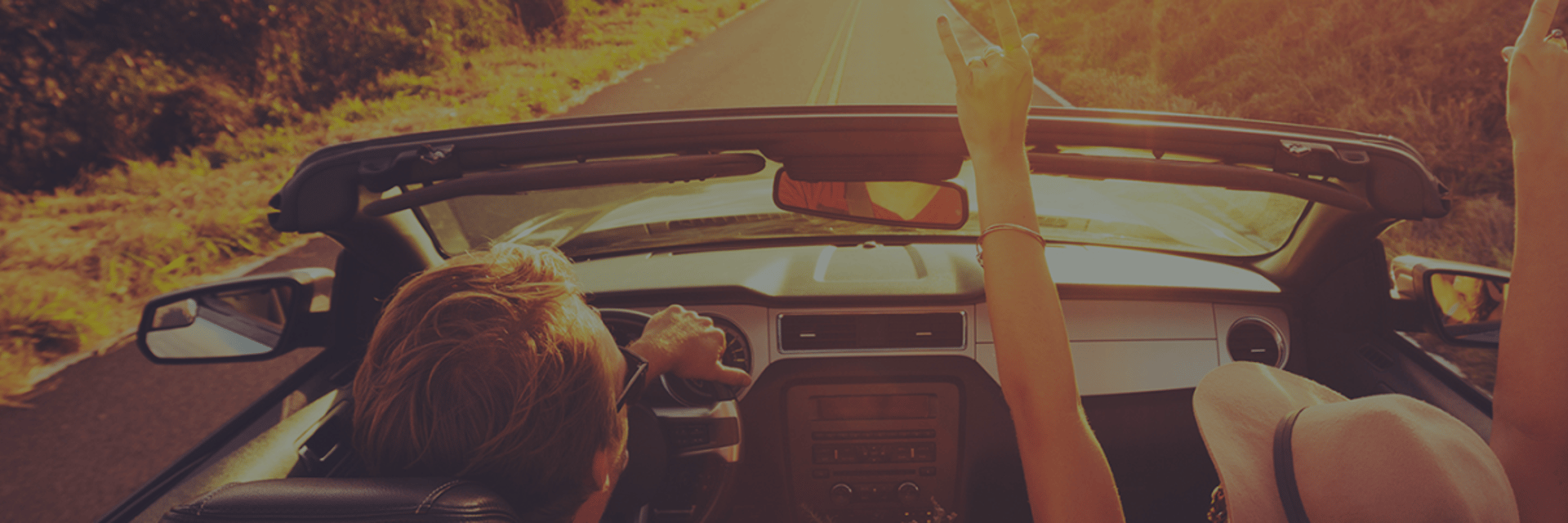 Driver and passenger in an open-top car on a coastal road at sunset